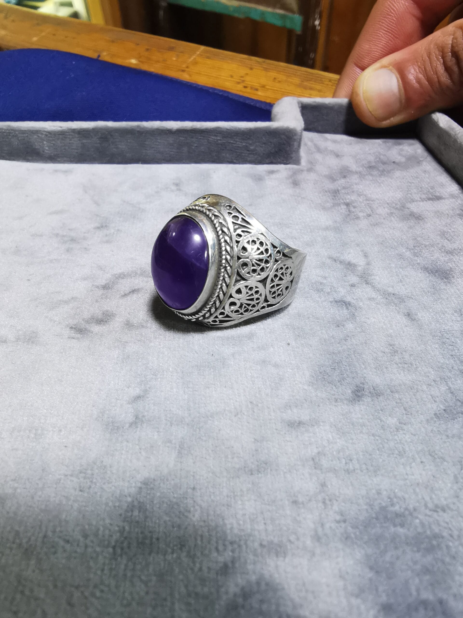 A beautifully crafted purple stone ring rests on a silver tray, highlighting intricate goldsmithing and Arabic artistic influences.